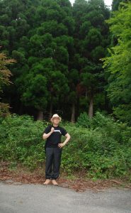 林の前に立つ坂本龍一氏の写真