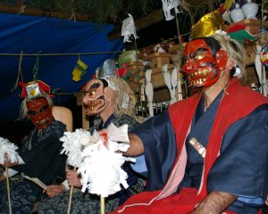 神面を被り、神楽の衣装を着た3人の荒神がおおぬさを持って座っている写真