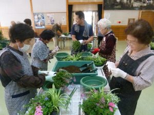 鉢植え講座で参加者達が台の上に乗せたプランターに花を植えている写真