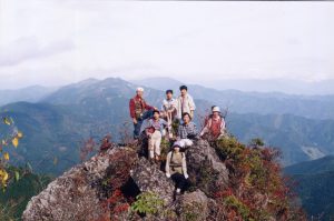山々が見渡せる黒岳展望台に登山者の方々が岩山に座って写っている記念写真