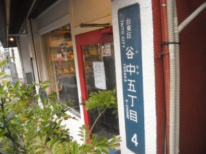 台東区谷中5丁目4としめされた住居番号表示板が店舗玄関横に表示されている写真
