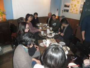飲み物や食べ物が置かれた4つのテーブルの周りにお客さんが席につき交流が行われている様子の写真