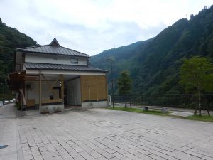 瓦屋根で2階建てのもろっこはうすの建物とマンホールの設置場所付近を写した写真