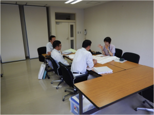 長机を向かい合わせに並べた席に座り、4名の関係者の方が話し合いをしている写真