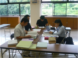 長机を向かい合わせに並べた席に4名の方が座り、資料などを見ながら話し合いをしている写真